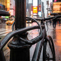 Schwarzes Master Lock Kabelschloss 8143 (8mm/1200mm) mit 4-stelligem Zahlencode sichert Fahrrad in NYC bei Regen.