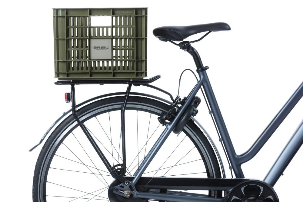 Grüne Basil Fahrradkiste M (29,5L) aus nachhaltigem Kunststoff auf dem Gepäckträger eines dunklen Fahrrads.