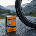 Continental Rennradschlauch Race 28" 700x20C-25C, 80mm Sclaverandventil, neben Rennrad auf nasser Bergstraße.
