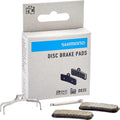 Shimano Scheibenbremsbelag D03S organisch. Produktbox mit zwei Bremsbelägen, Feder und Sicherungssplint.