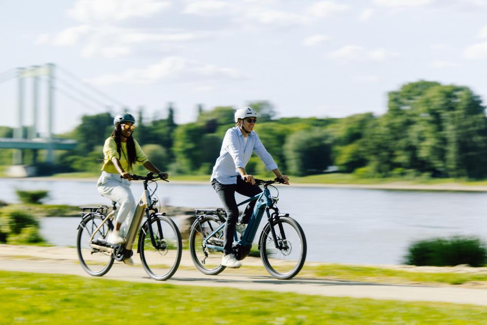 Zwei Personen radeln auf City-E-Bikes am Fluss, ausgestattet mit Schwalbe Motion Big Apple Reifen.