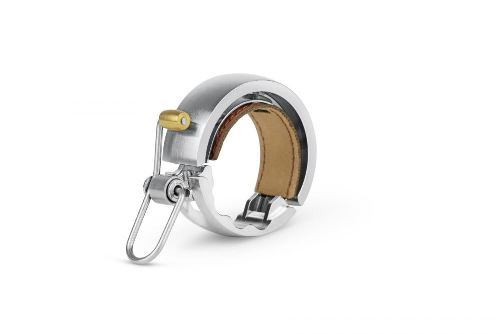 Knog Oi Luxe Fahrradklingel groß silber 23.8-31.8mm, mit Messinghebel und braunem Leder.