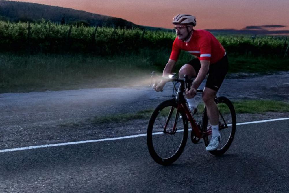 Radfahrer mit hellem Sigma Aura 80 USB Frontlicht bei Dämmerung auf der Straße.
