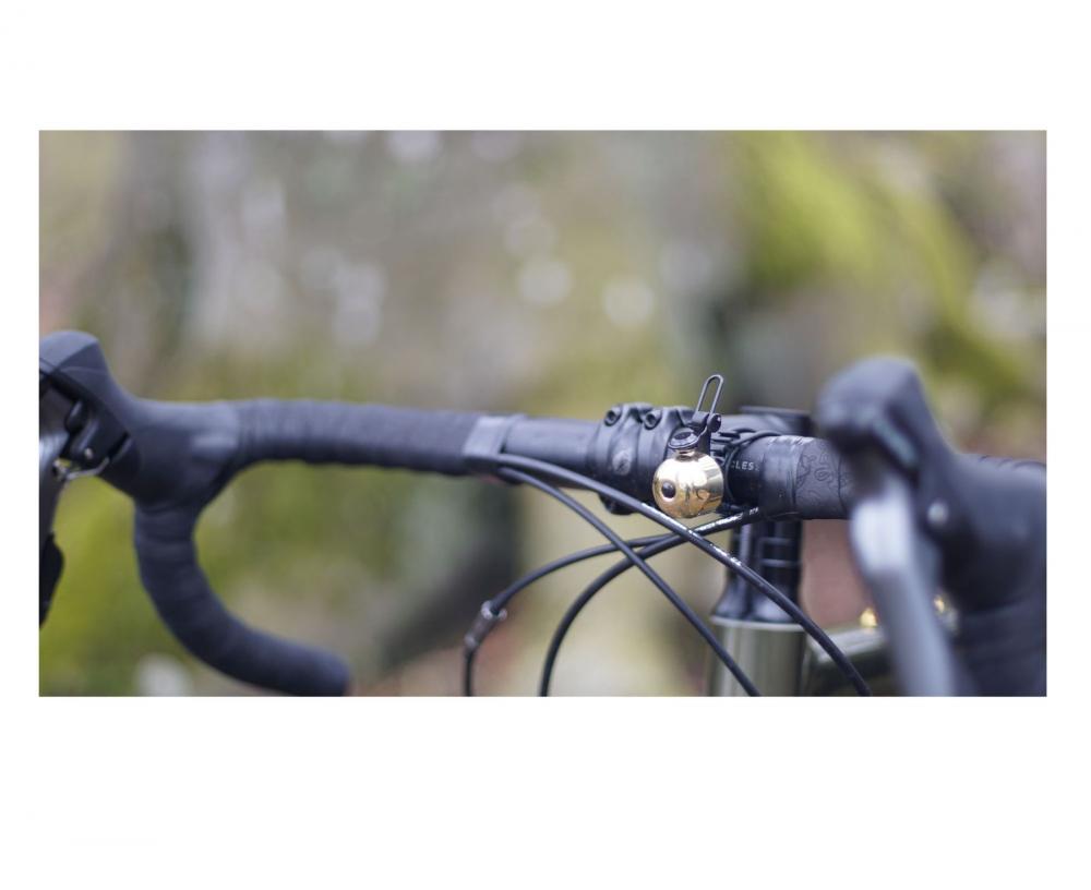 NG Sports Thian Fahrradklingel brass-black am Fahrradlenker, goldene Glocke mit schwarzem Hebel in Nahaufnahme.