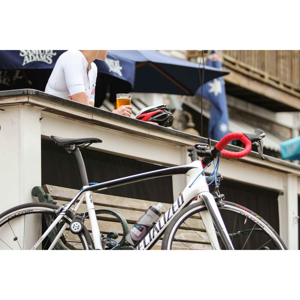 Kryptonite R2 einziehbares Kabelschloss schwarz am weißen Specialized Rennrad, Radfahrer pausiert mit Bier.