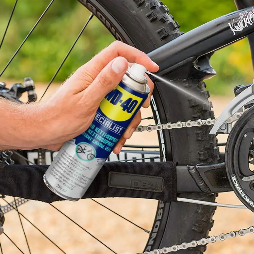 WD-40 Kettenspray 250 ml wird auf eine Fahrradkette gesprüht für Allwetter-Schmierung und Korrosionsschutz.