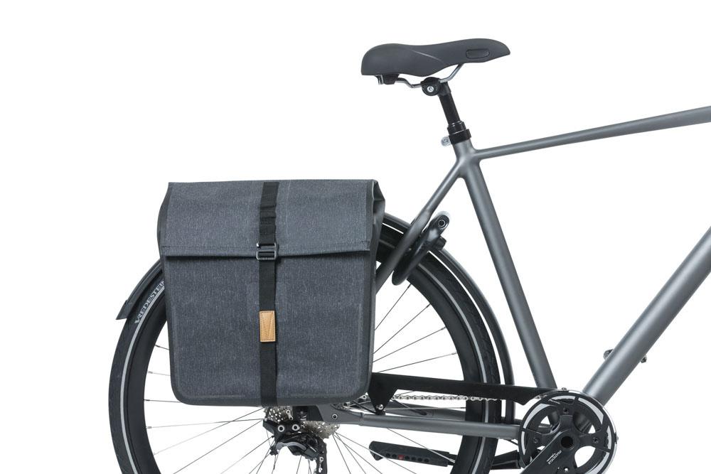 Graues Fahrrad mit großer anthrazitfarbener Basil Urban Dry Doppeltasche am Gepäckträger.