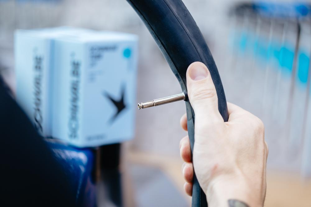 Hand hält Schwalbe Fahrradschlauch mit Ventil vor Schwalbe Verpackung.
